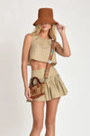 Woman wearing beige Nini top and skirt with a brown hat and bag on a white background