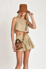 Woman wearing beige Nini top and skirt with a brown hat and bag on a white background