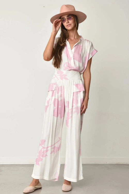 Woman wearing Kio top and pants in white with pink water lily pattern and a matching hat