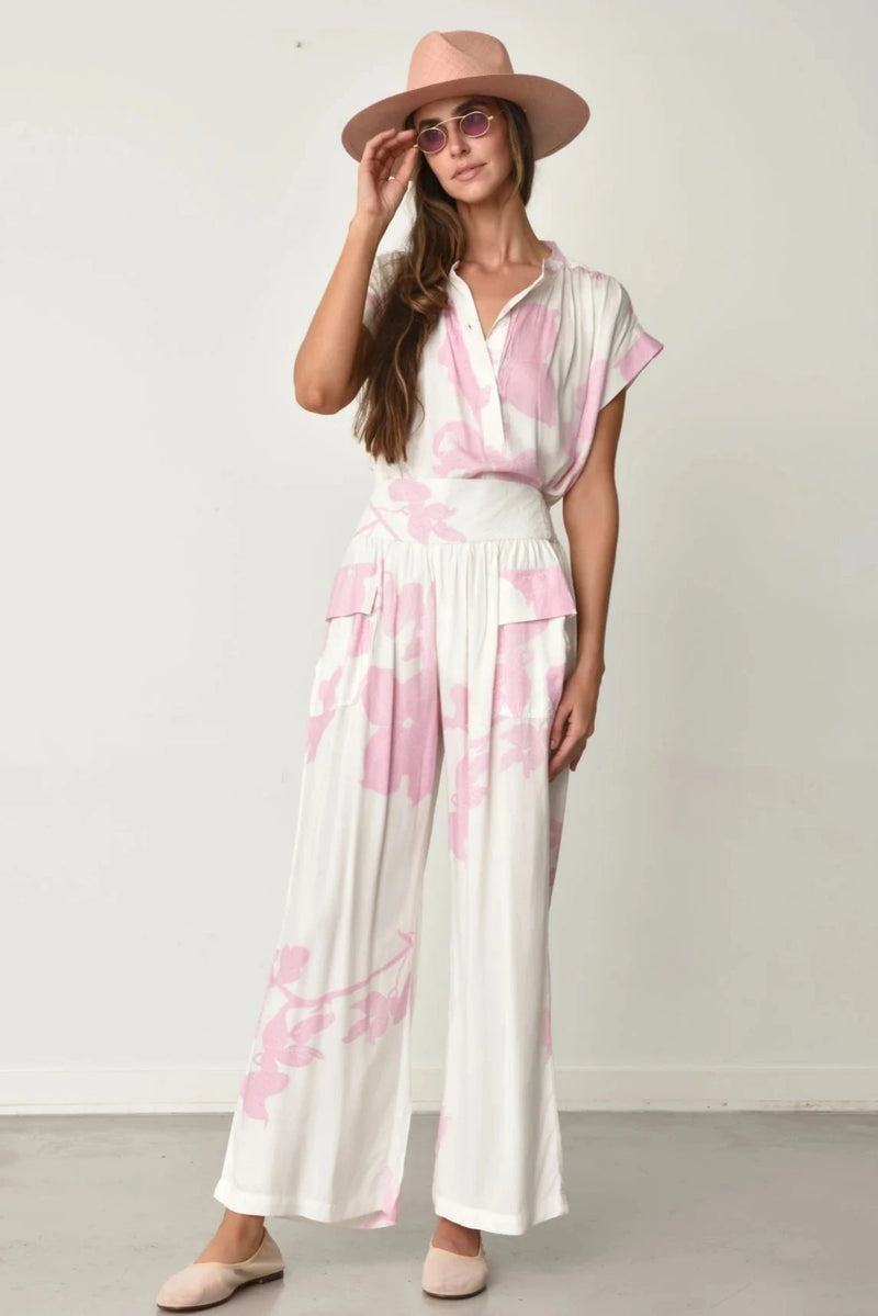 Woman wearing Kio top and pants in white with pink water lily pattern and a matching hat