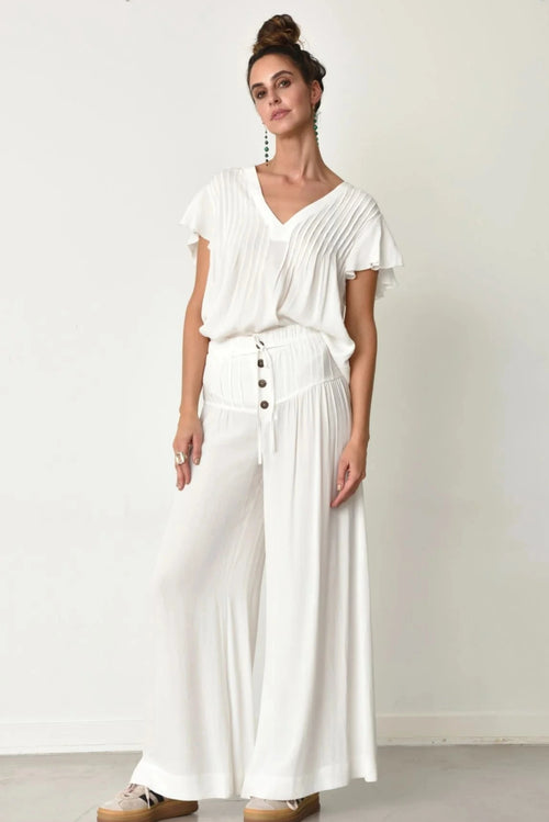 Woman wearing white Fany pants and white Hailey top with a plain background