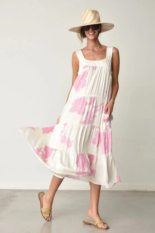 Woman wearing Kio white dress with pink water lily pattern and a hat on a plain background